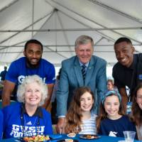 President Tom and Marcia Haas posing with guests sitting at a table at the Jamie Hosford Football Center dedication.